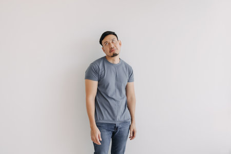 Disappointed and bored face of asian man in blue t-shirt stand isolated on white wall.の写真素材