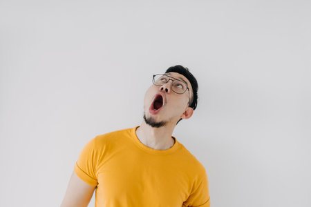 Shocked surprised face asian man yellow t-shirt eyeglasses isolated on white.の写真素材