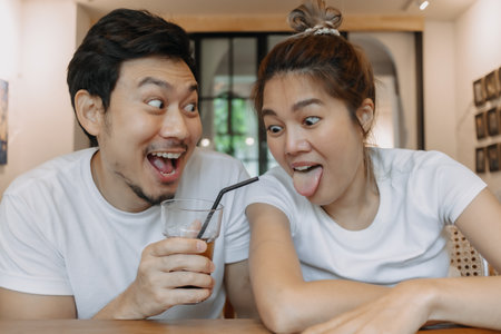 Funny faces lovely Asian couple man and woman in white t-shirt in coffee shop.の写真素材
