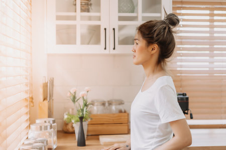 Asian woman looking out the window from white warm kitchen.の写真素材