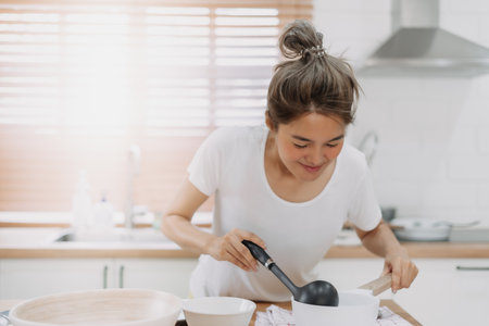 Happy asian woman cooking and smell the soup, preparing meal for husband.の写真素材
