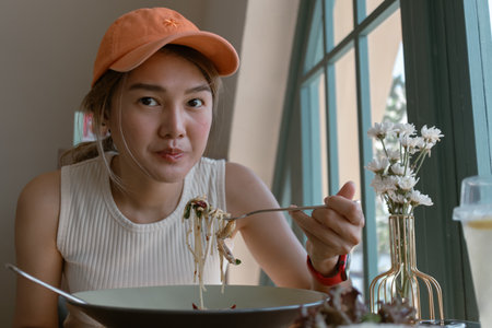 Asian woman wears orange cap eating spaghetti in the cafe.の写真素材