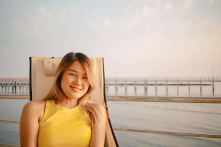 Happy asian woman is reading post in social application on the phone while relaxing on holiday at the sea.の写真素材