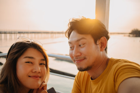 Happy Asian couple lover take selfie photo in the resort with romantic sunset at the sea.の写真素材