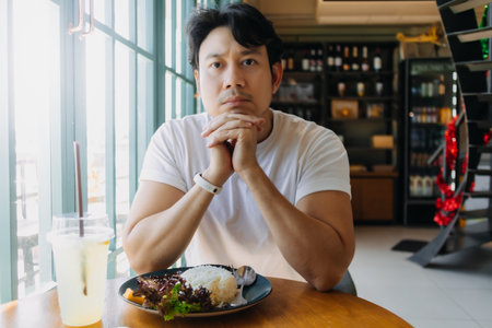 Asian man in white t-shirt is waiting for someone to meet at the restaurant with Thai food.の写真素材