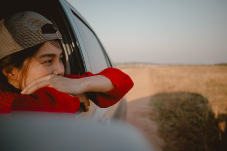 Young Asian woman in red sweater leaning out of car window looking out to the field.の写真素材