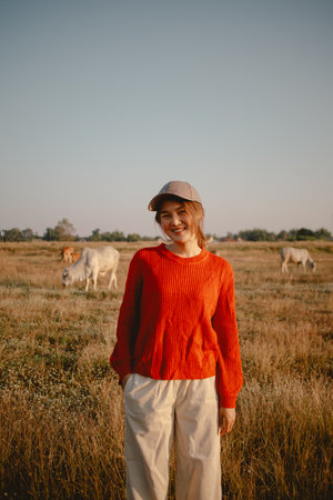 Happy asian woman in red sweater walking on the grass field to see the cows cattle and the sunset view.の写真素材