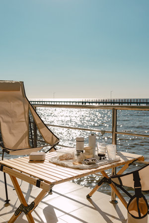 Set of picnic camping with folding chair and table, Manual grinder and coffee press, beautiful bright sky and ocean vacation.の写真素材