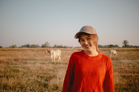 Happy asian woman in red sweater walking on the grass field to see the cows cattle and the sunset view.の写真素材