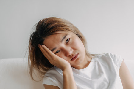 Close up headshot of headache hangover Asian woman with hand covering her head.