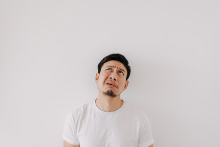 Funny bored and disappointed face Asian man in white t-shirt isolated on white wall.の写真素材