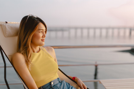 Happy Asian woman sits and relaxed enjoy sunset sea view of her honeymoon.の写真素材