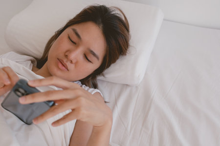 Asian woman browsing and checking social media feed in her mobile phone, can not sleep and stay awake.の写真素材
