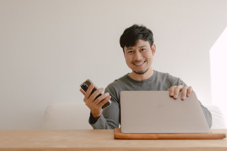 Happy Asian man working on computer feeling happy with the app in mobile phone.の写真素材