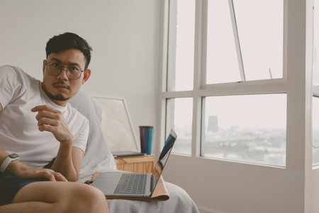 Asian man woking boring job with computer in his room sitting on the sofa.の写真素材