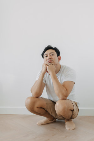 Bored face Asian man squatting on the floor with white wall.の写真素材