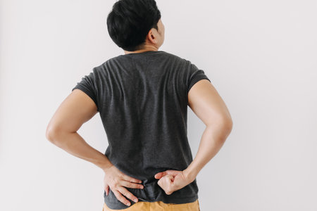 Asian man in black t-shirt feeling sick and hurt of back pain isolated on white wall.