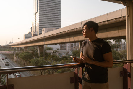 Asian man is using mobile phone while walking on the sky train platform in Bangkok.