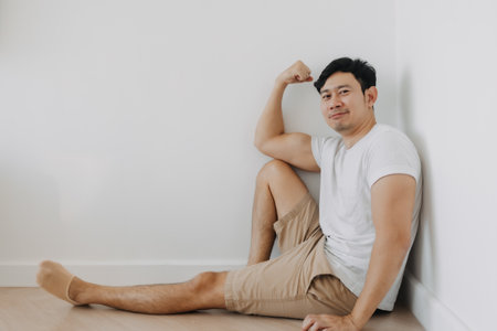 Happy laughing Asian man is sitting casually at the corner of the room.の写真素材