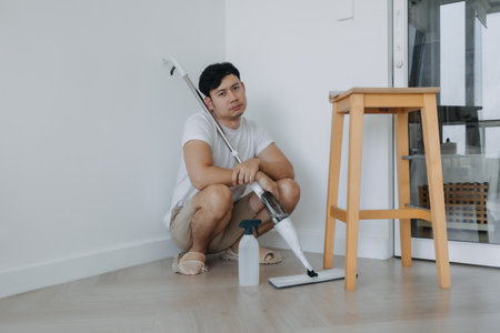 Tired househusband asian man sit on the floor after mopping the room.の写真素材