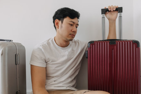 Sad disappointed asian man sit with his luggages as his traveling trip plan has been cancelled.の写真素材