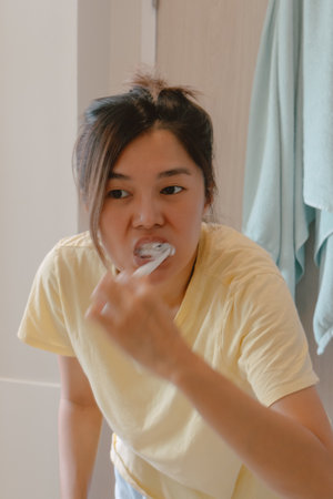 Asian Thai woman holding toothbrush and using toothpaste brushing her teeth, looking at the mirror,...