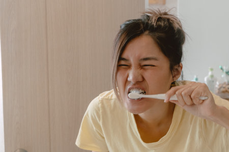 Asian Thai woman holding toothbrush and using toothpaste brushing her teeth, looking at the mirror, daily routine, keep cleaning.の写真素材