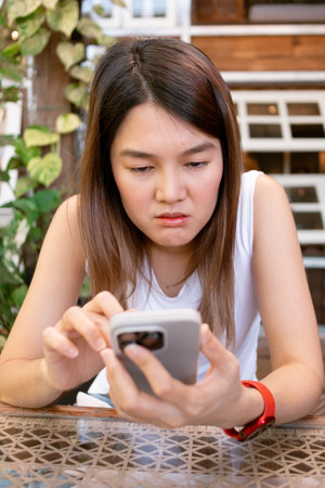 Vertical photo of Asian woman browsing social media in mobile, feeling sad and depress.の写真素材
