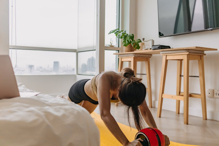 Asian woman workout exercise with red ab wheel and yellow mat in the room.の写真素材