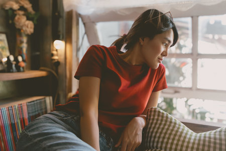 Sleepy asian woman in red t-shirt resting in the living room near the windows.の写真素材
