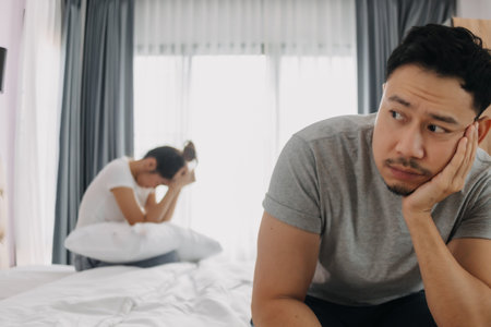 Asian couple lover, husband sad and sulking sit on the bed and wife turning backの写真素材