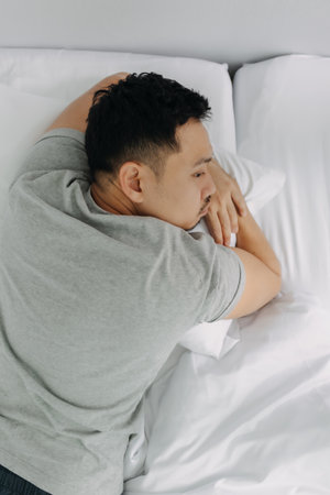 Serious and depressed asian man overthinking the problems lying on the bed.の写真素材