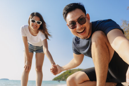 Playful asian couple lovers taking photo together at the beach, low angle.の写真素材