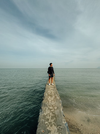 Asian man walking alone on the breakwater to see the view of the ocean.の写真素材