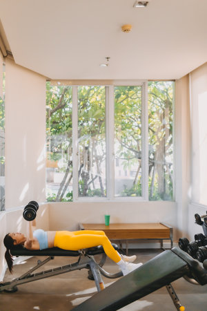 Asian woman in Blue Yellow outfit does Dumbbell Bench Press for chest workout.の写真素材