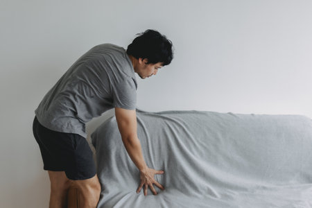 Asian man is doing his house work, covering the sofa with grey sheet.の写真素材