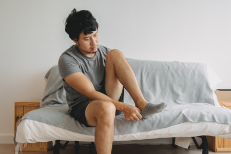 Asian man in grey t-shirt wearing socks in the living room of his apartment.の写真素材