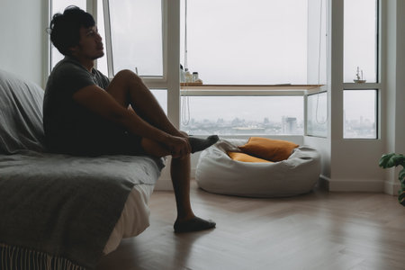 Asian man in grey t-shirt wearing socks in the living room of his apartment.の写真素材
