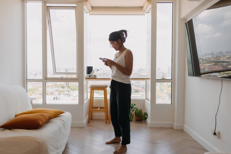 Asian woman walking around her room and chat with the mobile phone.の写真素材
