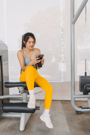 Asian woman in yellow blue fitness using phone while resting between training.の写真素材