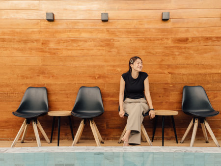 Happy Asian woman enjoy sitting outdoor at the swimming pool with wooden wall.の写真素材