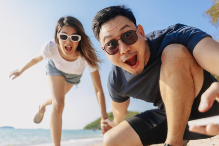 Playful asian couple lovers taking photo together at the beach, low angle.の写真素材
