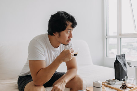 Vacant absent minded Asian man staring out the windows, holding a coffee cup.の写真素材