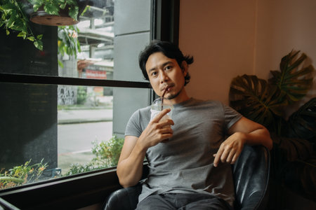 Happy Asian man relaxed in the cafe, drinking iced coffee.の写真素材