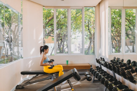 Asian woman in Yellow Blue fitness outfits picking up the dumbbells in the gym.の写真素材