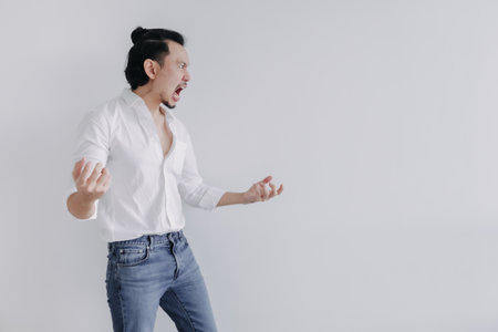 Angry face of long hair Asian man bun in white shirt and jean stand on white.の写真素材