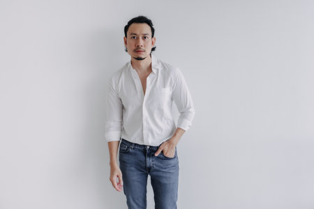 Pensive face long hair Asian man bun in white shirt and jean stand on white.の写真素材