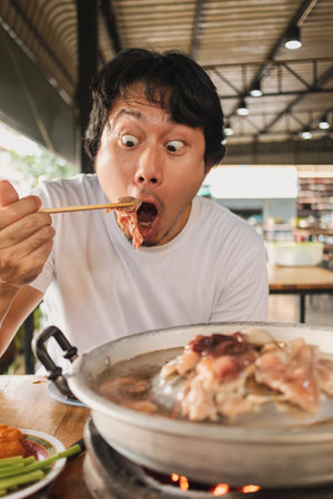 Happy and excited Asian face man eating Moo Kra Ta or Thai BBQ buffet.の写真素材
