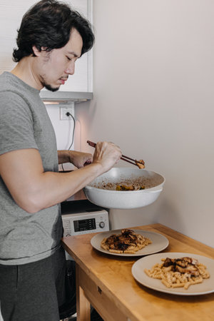 Asian man preparing two dishes of homemade pasta in his small kitchen.の写真素材