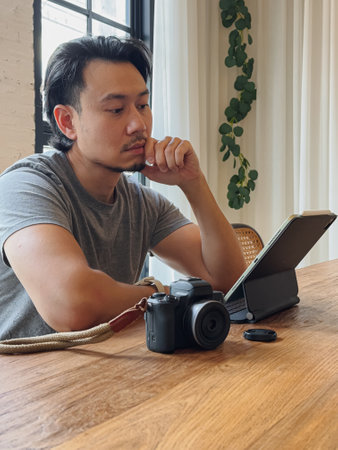 Serious photographer Asian man work with his computer tablet at the wooden desk.
